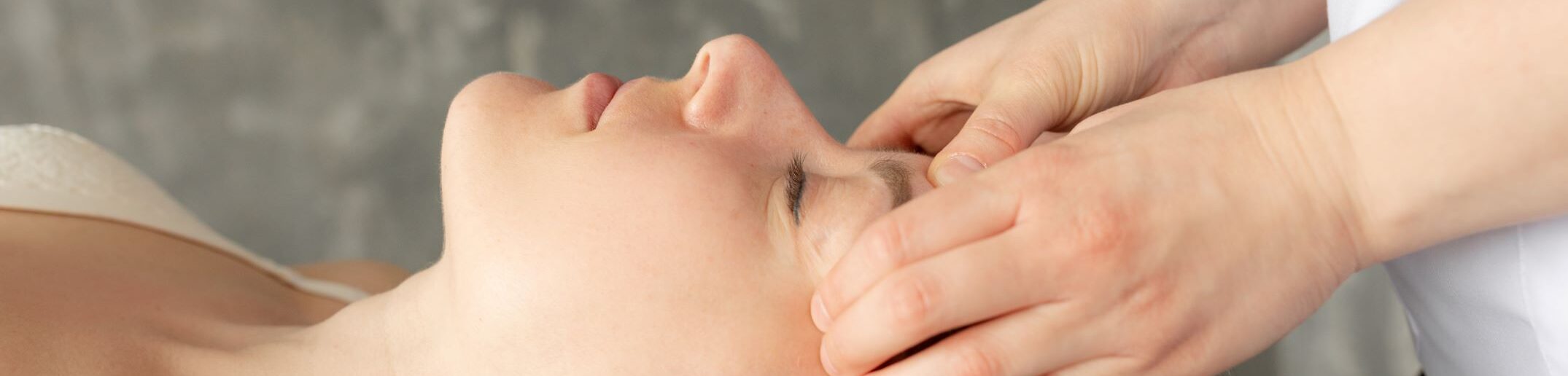 Craniosacral Therapie: Frau liegt mit geschlossenen Augen auf einer Behandlungsliege, während ihre Stirn sanft mit den Händen einer Therapeutin berührt wird.