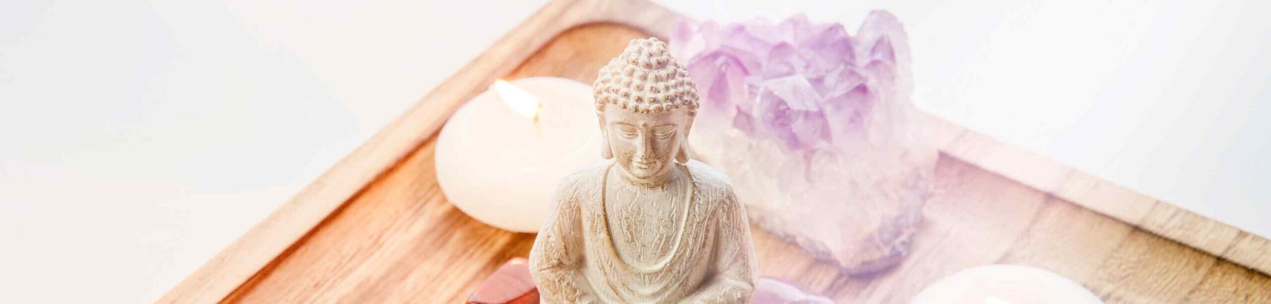 Buddha-Figur umgeben von Heilsteinen und brennenden Kerzen – Symbol für Chakra-Balance, Achtsamkeit und energetisches Gleichgewicht.