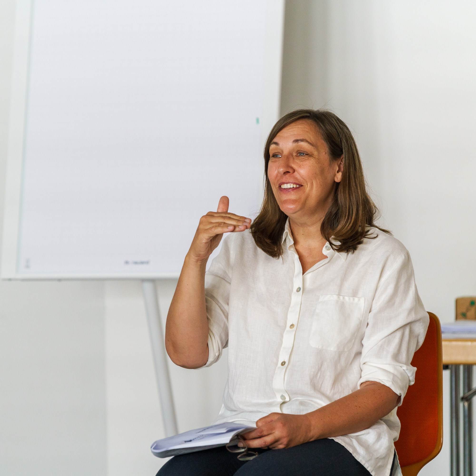 Dozentin bei APAMED erklärt sitzend und gestikulierend ein Thema während einer Unterrichtseinheit.