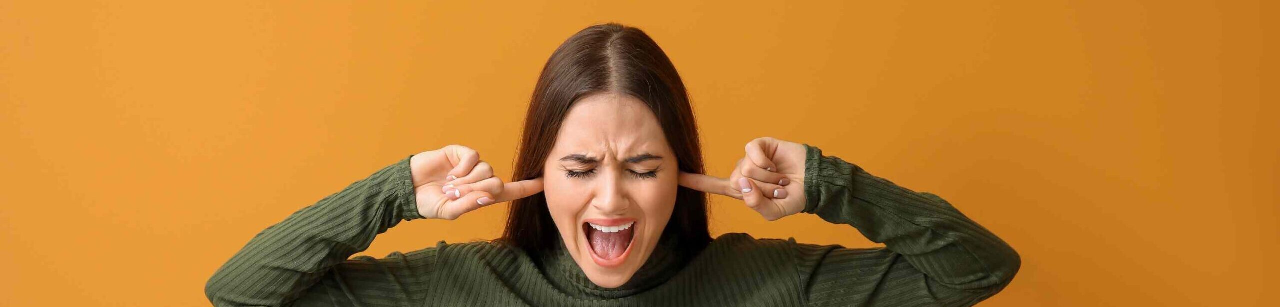 Frau hält sich gestresst die Ohren zu – Symbolbild für Tinnitus und Überreizung