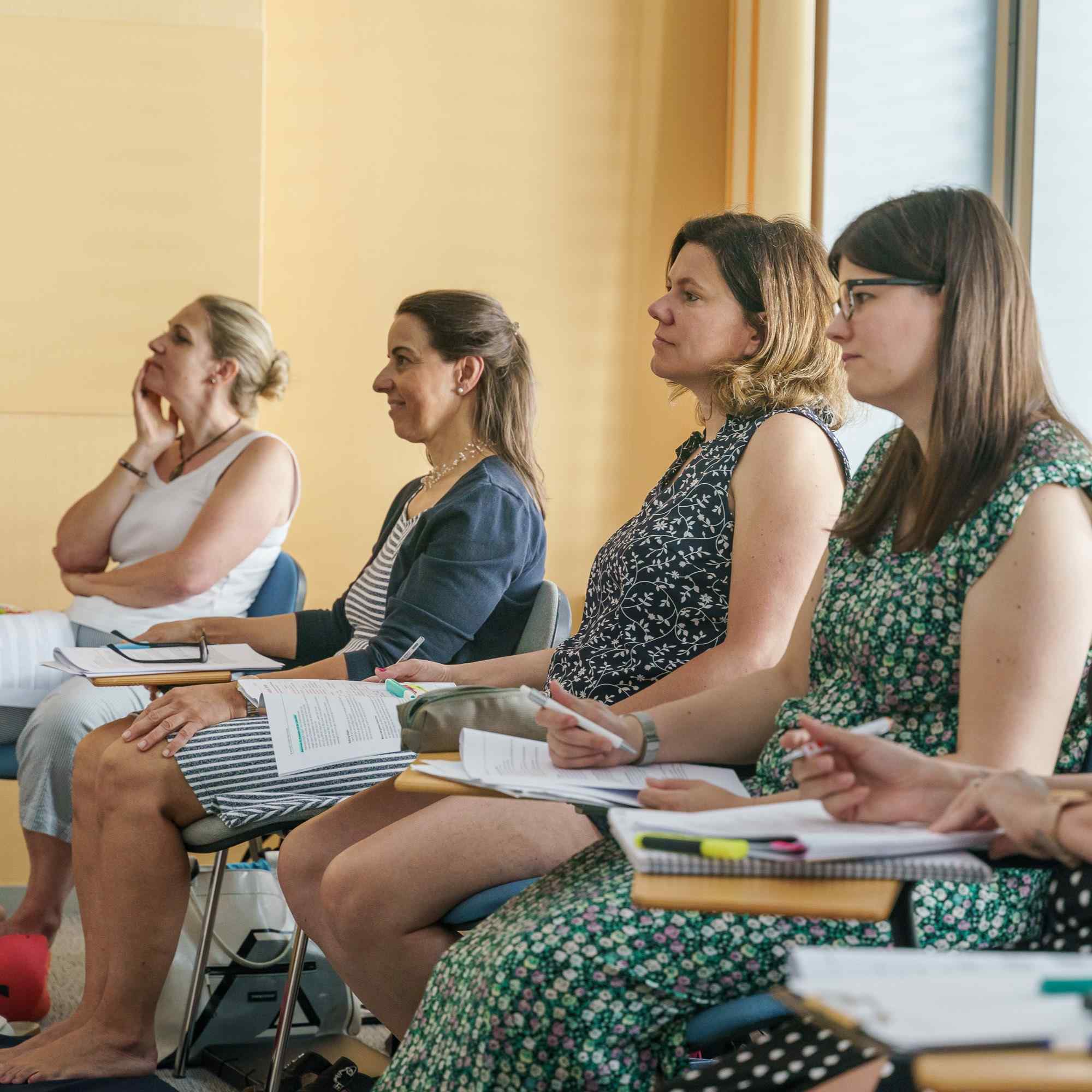 Fünf Frauen sitzen konzentriert im APAMED-Unterricht und machen sich Notizen in ihren Ausbildungsunterlagen.