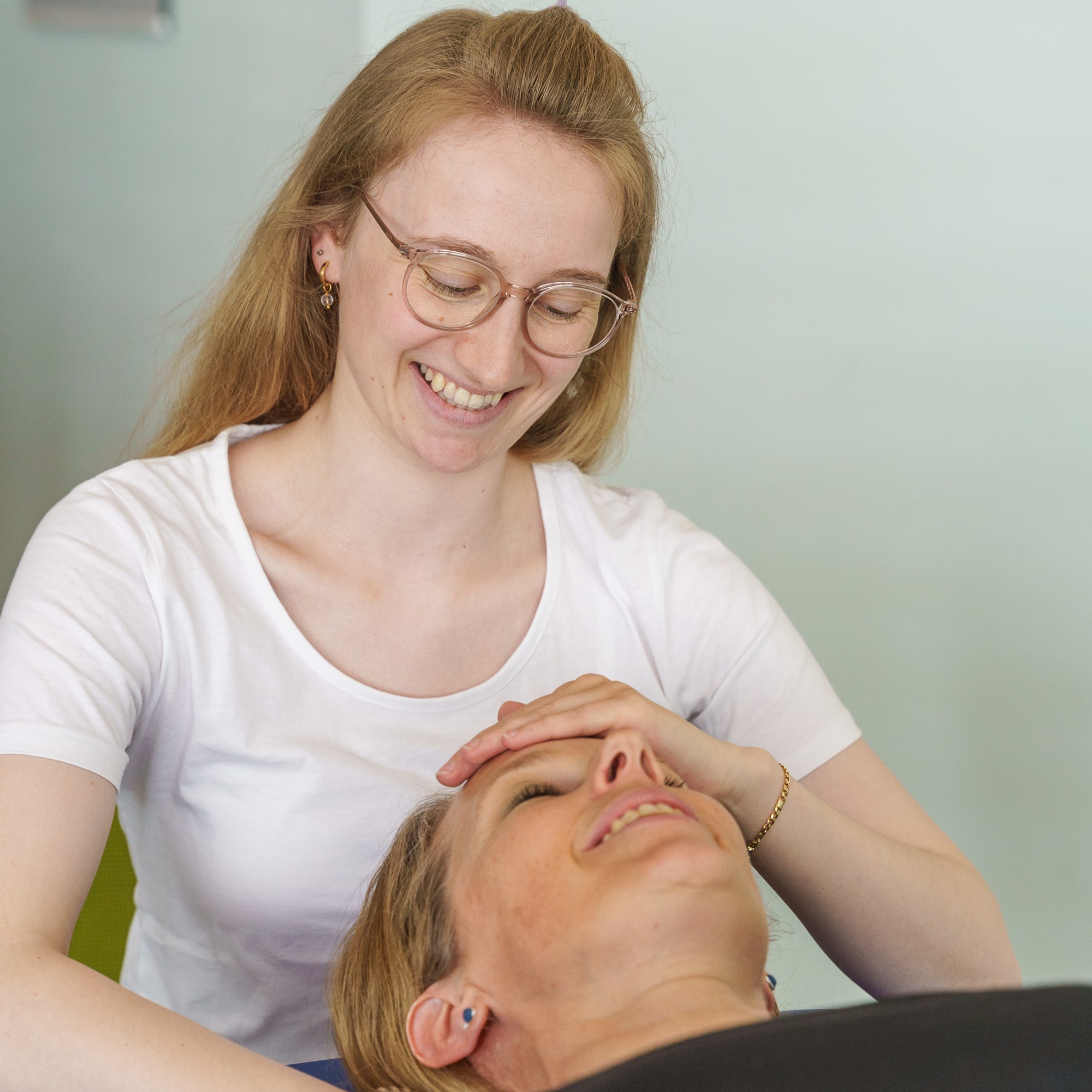 Craniosacral Therapie: Junge Therapeutin legt einer Klientin sanft die Hand auf die Stirn während einer Behandlungssituation bei APAMED.