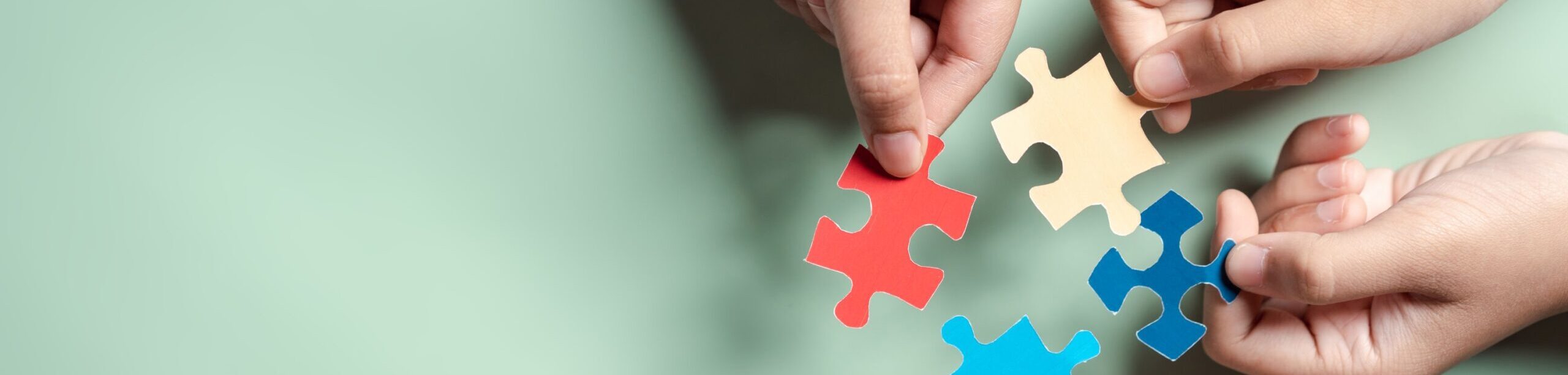 Vier Hände halten farbige Puzzleteile – Symbol für Zusammenarbeit und Lösungsfindung