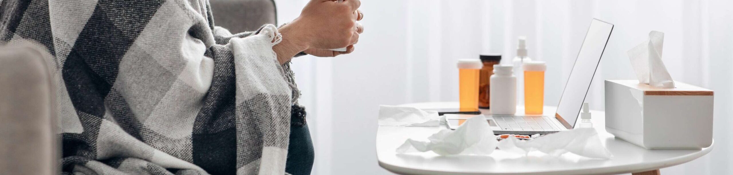Mann mit Decke, Tasse und Medikamenten am Tisch – Symbolbild für Krankheit und Therapiebegleitung