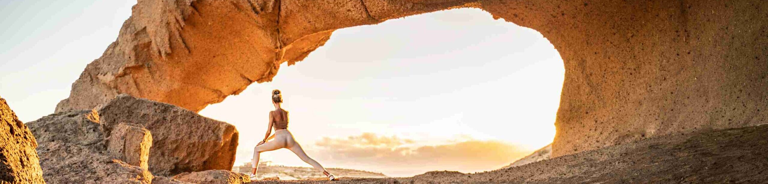 Frau in Yoga-Pose vor Felsformation im Sonnenaufgang – Symbol für innere Balance und energetische Regeneration