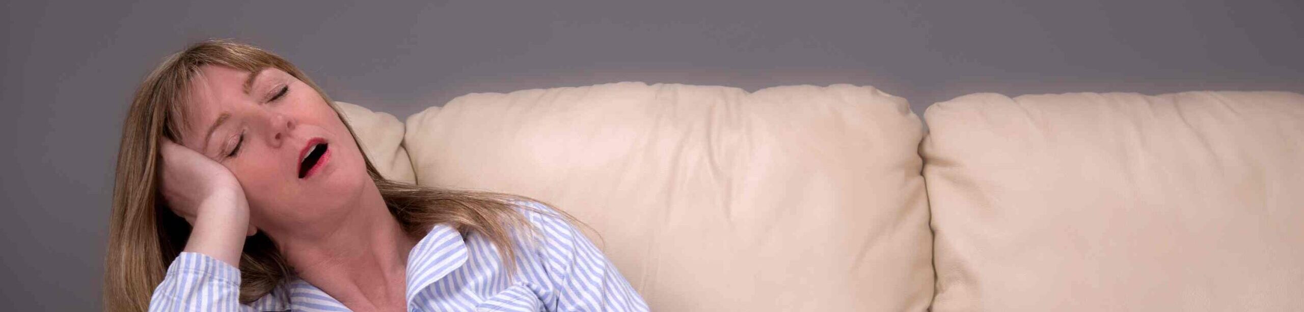 Frau schläft im Pyjama auf dem Sofa und schnarcht mit offenem Mund