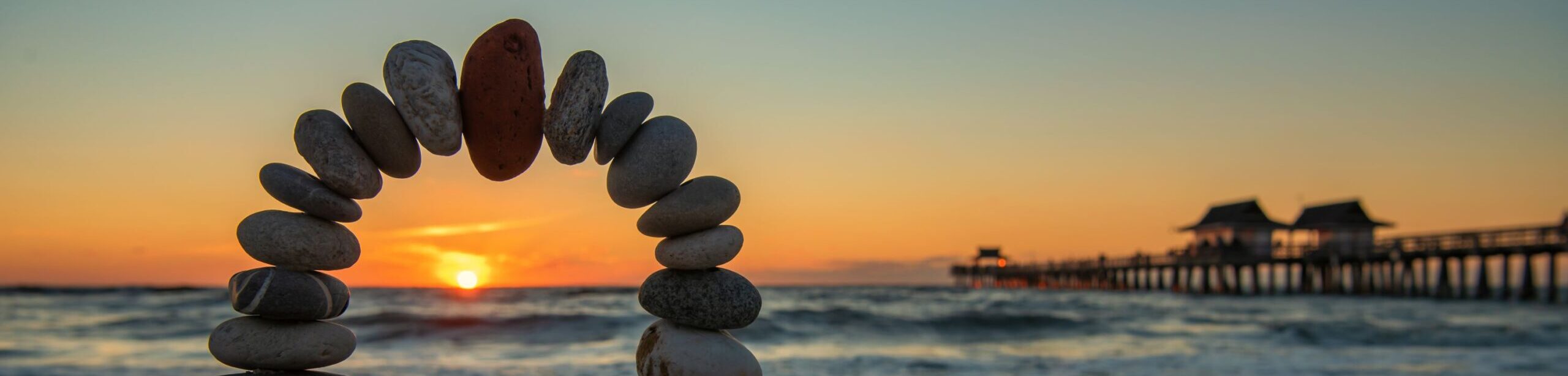 Balancierter Steinkreis vor Sonnenuntergang am Meer – Symbol für innere Stabilität und emotionale Ressourcen