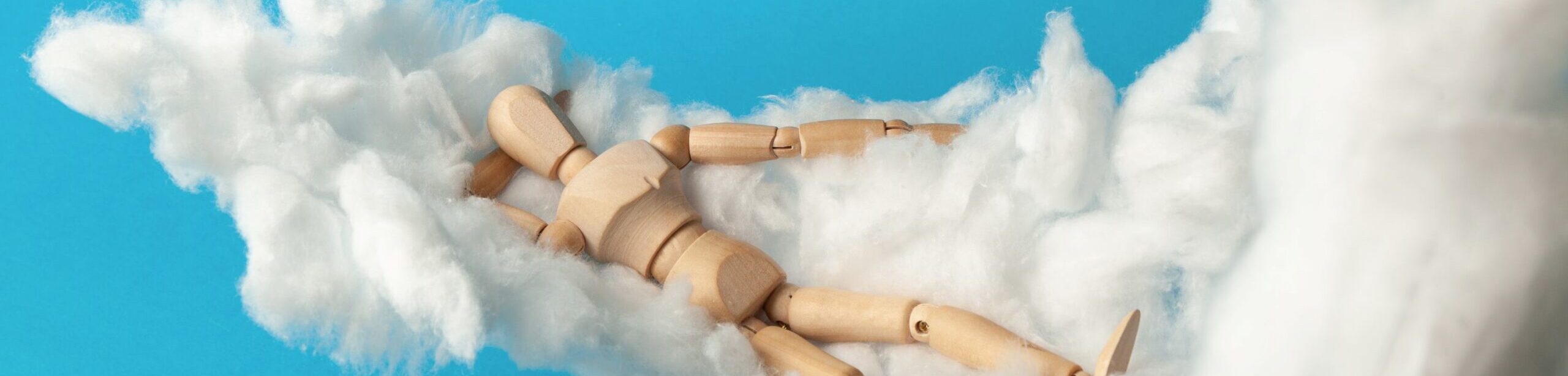 Holzfigur liegt träumend auf Wattewolken – Symbolbild für Tiefenpsychologie und Traumwelt