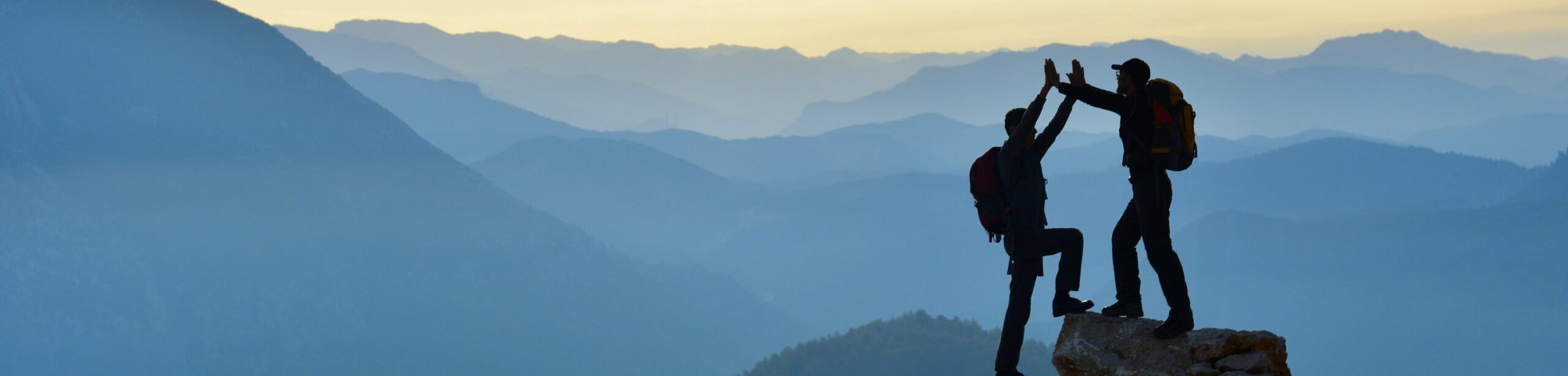 Zwei Menschen geben sich auf einem Gipfel ein High-Five vor Bergpanorama – Symbol für gemeinsames Wachstum