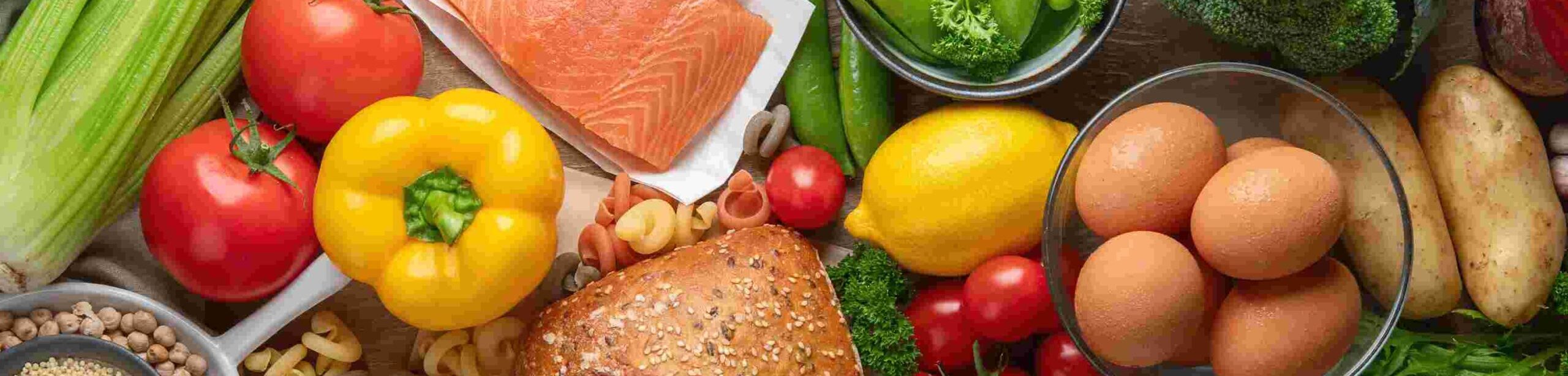 Ausgewogene Auswahl an Vollwert-Lebensmitteln mit Getreide, Gemüse, Fisch, Hülsenfrüchten und Eiern auf einem Holztisch