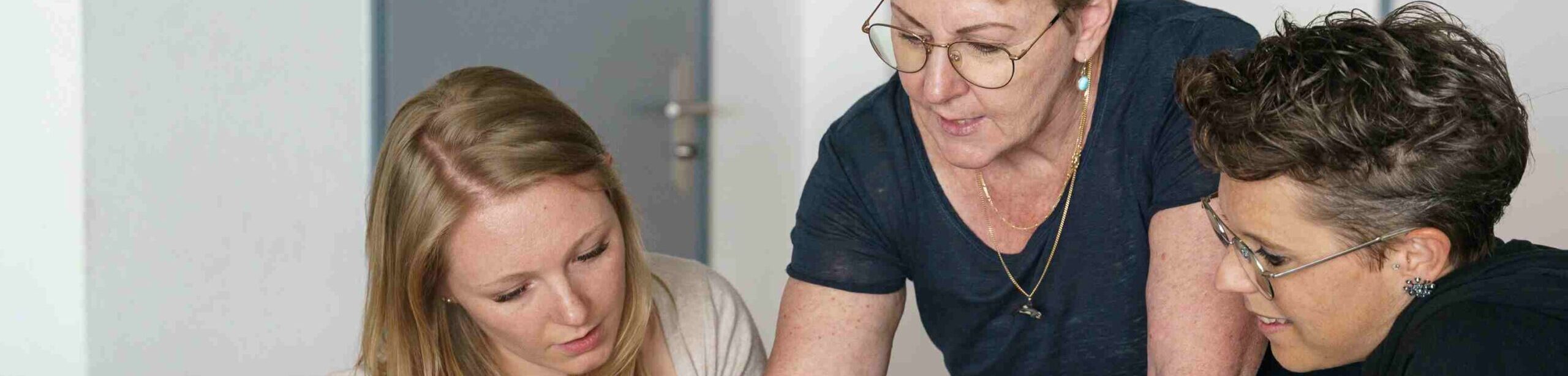 Dozentin erklärt zwei Studierenden ein Thema anhand von Schulungsunterlagen während einer Unterrichtseinheit bei APAMED.