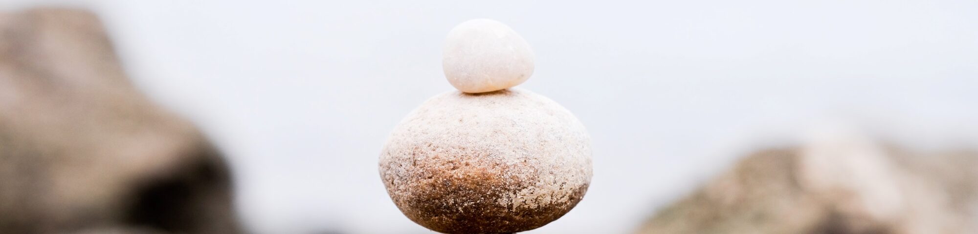 Zwei übereinander balancierte Steine auf einem Fels – Symbol für innere Balance, Resilienz und Gelassenheit bei Belastungen.